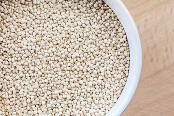 Raw organic quinoa seeds in white cup on wooden board background