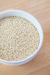Raw organic quinoa seeds in white cup on wooden board background