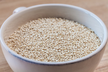 Raw organic quinoa seeds in white cup on wooden board background
