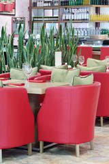 Tables with glasses, red armchairs and green leaves