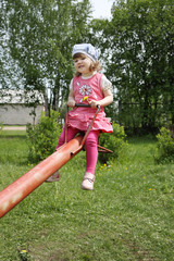 Happy little cute girl in pink rides on red seesaw at summer day