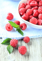 Ripe sweet raspberries in bowl on wooden background