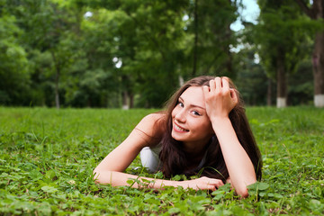 Naklejka na ściany i meble Smiling young woman lying on green grass