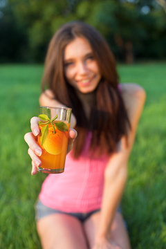 Young smiling woman sitting on the grass with glass of orange ju