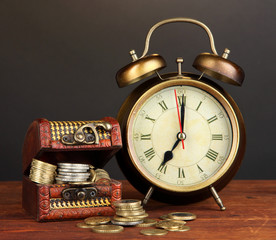 Antique clock and coins on wooden table on black background