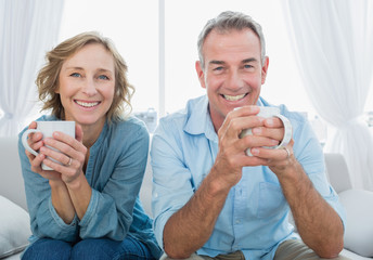 Smiling middle aged couple sitting on the couch having coffee