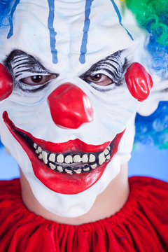 Scary clown person in clown mask on blue background