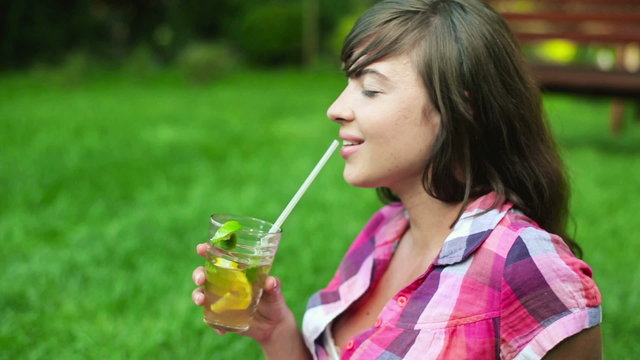 Portrait of happy young woman drinking lemonade in park