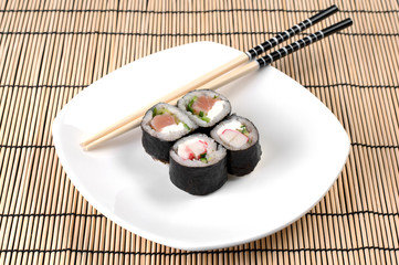 Delicious sushi rolls on white plate with chopsticks