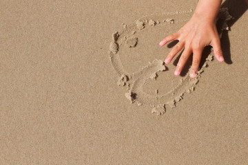Fototapeta na wymiar Kid hand drawing a heart in the sand