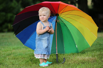 Cute baby girl standing under colorful umbrella