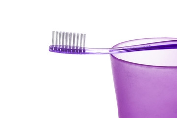 A purple toothbrush lies on a cup on white