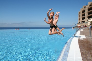 Two happy twin brothers are jumping into infinity swimming pool