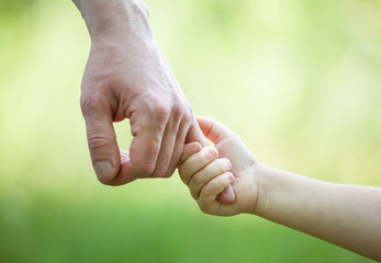 : Hands of man and child holding together on light green backgro