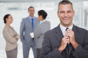 Smiling manager tidying his tie up with employees in background