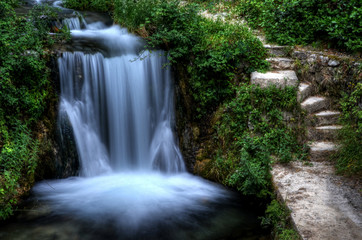 Fototapeta na wymiar Steps next to a waterfall in green garden