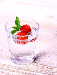 Water in glass with two raspberries and mint