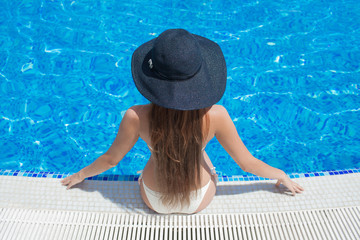 Young beautiful woman sitting on the ledge of the pool in black