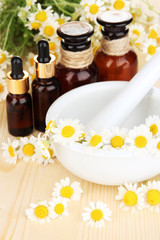 Essential oil and chamomile flowers in mortar on wooden table