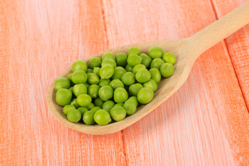 Sweet green peas in spoon on wooden background