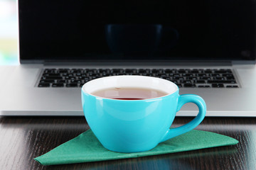Blue cup on napkin on laptop background on wooden table