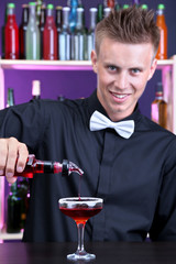 Portrait of handsome barman preparing cocktail, at bar