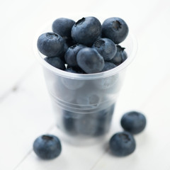 Ripe blueberries in a plastic cup on white wooden boards