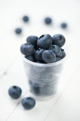Plastic cup full of fresh blueberries on white wooden boards