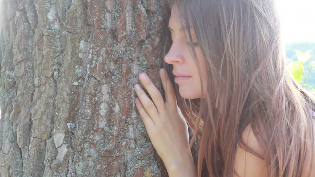 Happy beautiful girl hugging big tree in park