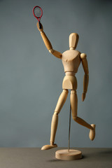 Wooden mannequin with tennis racket on grey background