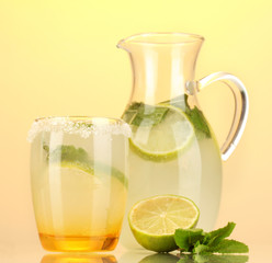 Lemonade in pitcher and glass on yellow background