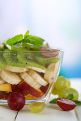 Tasty fruit salad in glass bowl, on white wooden table