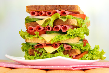Huge sandwich on wooden table, on light background