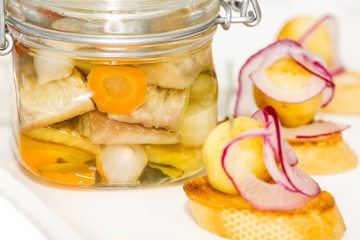 pickled herring in a glass jar with potato canapes