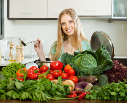 happy blonde woman cooking with heap of  vegetables