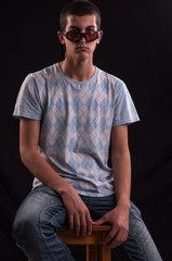 Obraz premium Serious young caucasian man with sunglasses sitting on chair