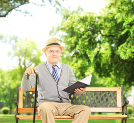 Senior man sitting on a wooden bench and reading a book