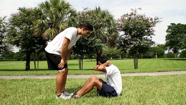 Young man doing sit-ups, exercising with personal trainer