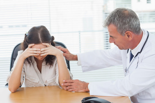 Serious doctor comforting his patient after telling her diagnosi