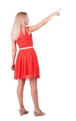Back view of young blonde woman pointing at wall.
