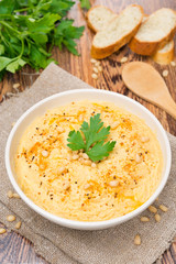 Hummus with pine nuts in a bowl, vertical, top view