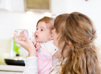 Obraz na płótnie Canvas Mother feeding baby with feeding bottle in kitchen