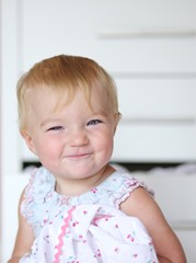 Funny smiling little girl in dress in front of white commode