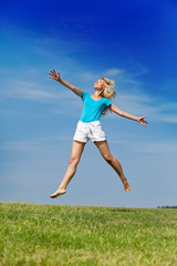 Fototapeta na wymiar happy woman jumps in a summer green field against blue sky...