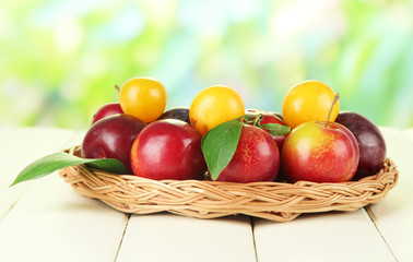 Ripe plums in basket on wooden table on natural background