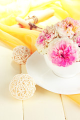 Roses in cup on wooden table on yellow cloth background