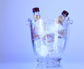 Minibar bottles in bucket with ice cubes,  on color background
