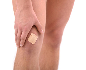 Young man with adhesive bandage on knee, isolated on white