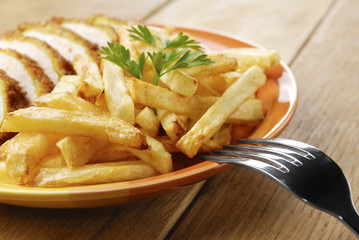 French fries and chicken on the plate on the wooden table