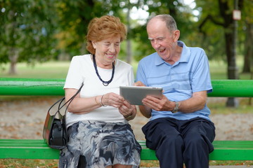 Two senior people sitting with a tablet PC in a nature park © Visionsi